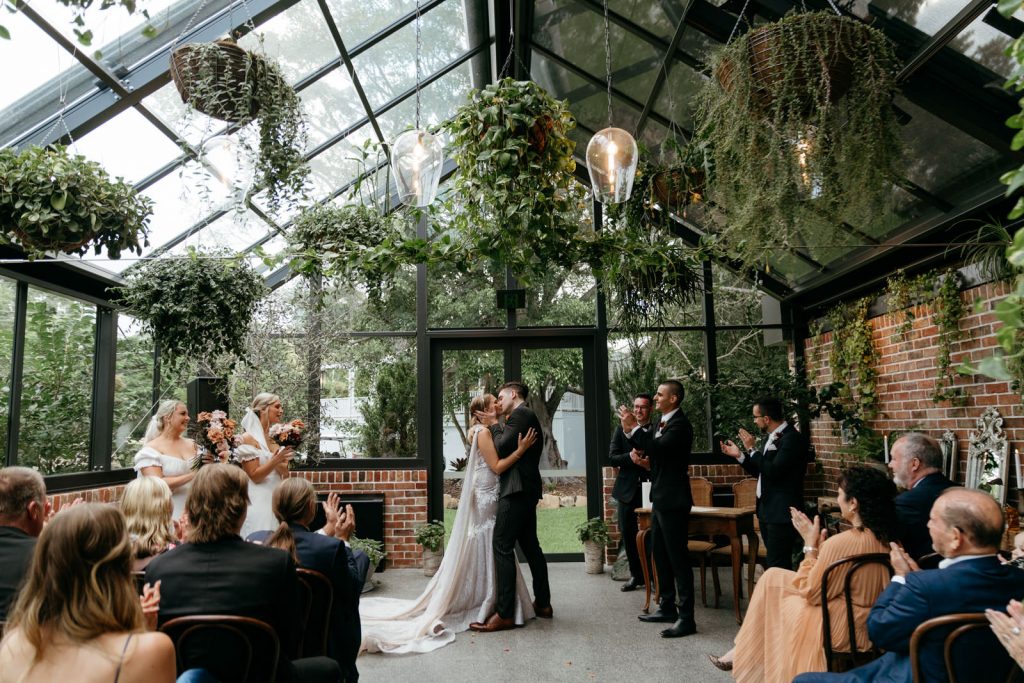 Bride and groom first kiss at The Valley Estate Glasshouse room